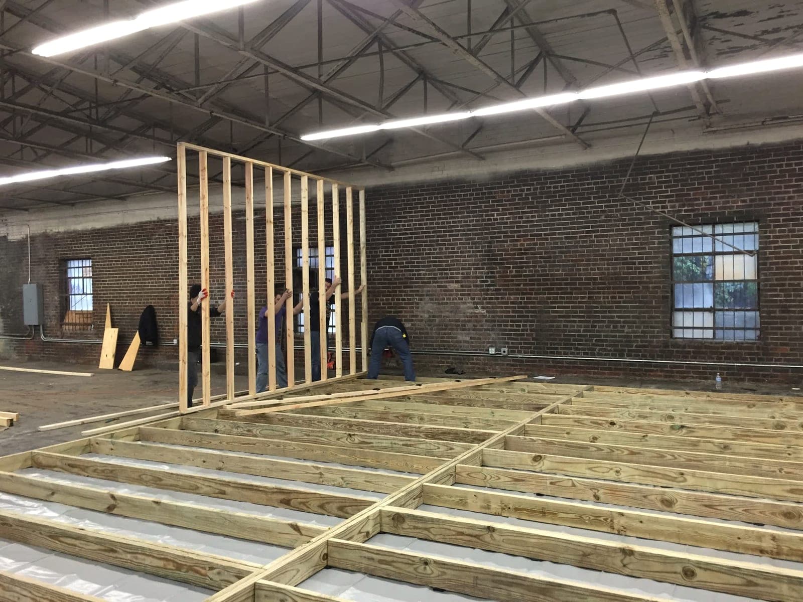 Four friends raise the first framed stud wall inside the warehouse.